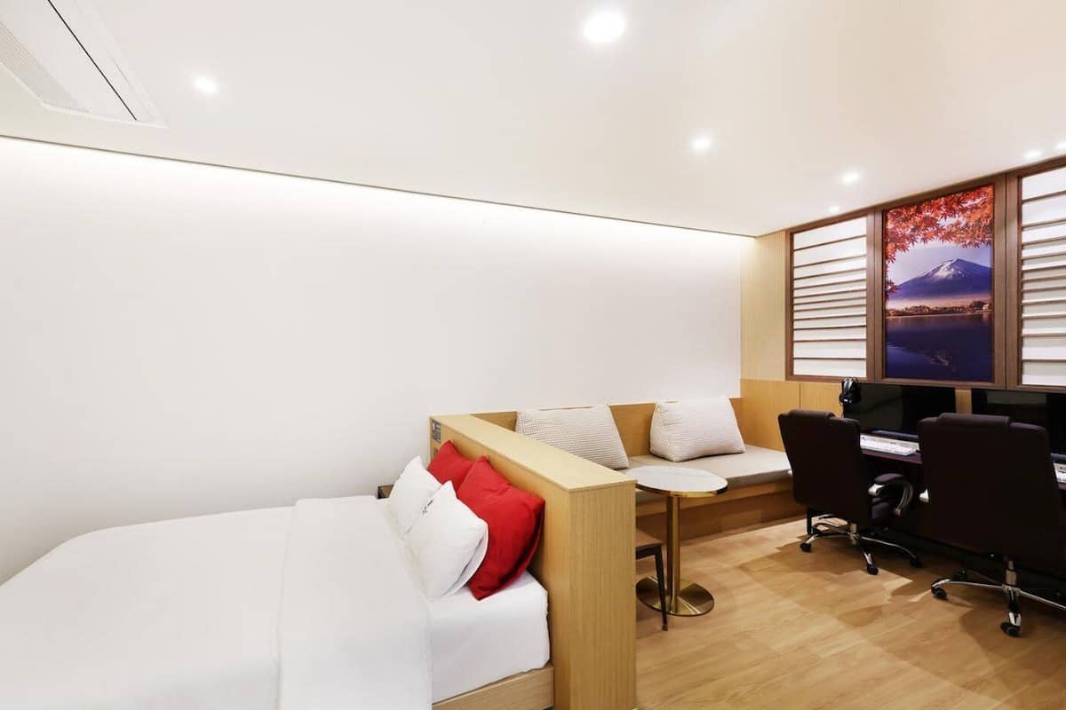 A modern hotel room with a bed, a desk, and a computer setup.