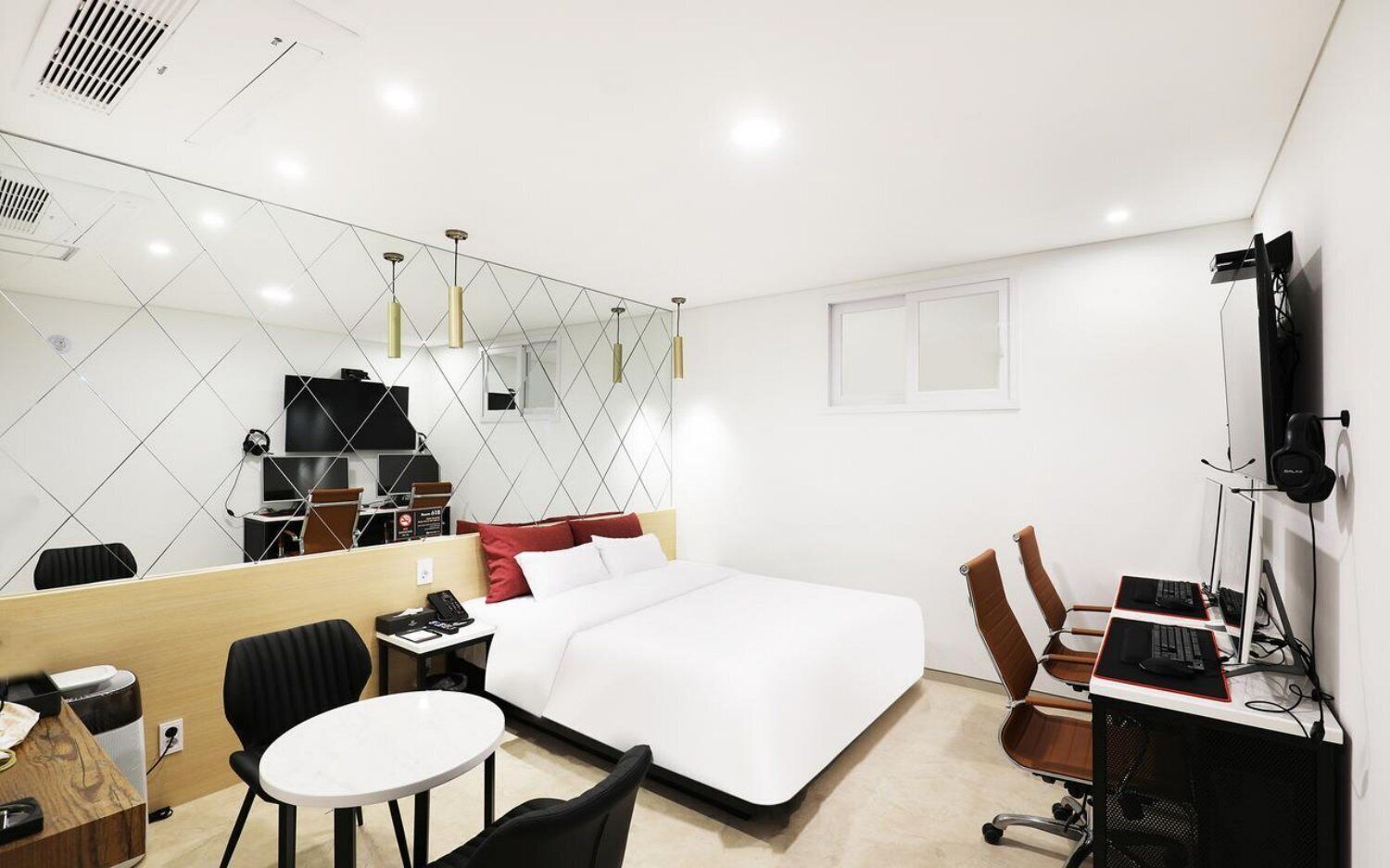 A hotel room with a bed, a desk with a computer, a chair, a small table, a mirror, and a TV.