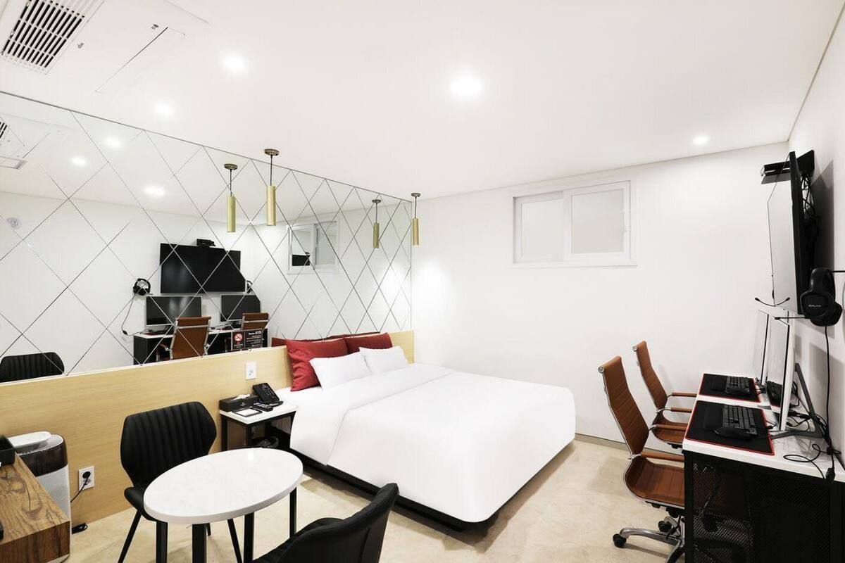 Une chambre d’hôtel comprenant un lit, un bureau avec un ordinateur, une chaise, une petite table, un miroir et un téléviseur.