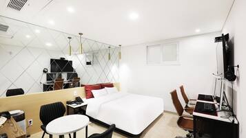 Une chambre d’hôtel comprenant un lit, un bureau avec un ordinateur, une chaise, une petite table, un miroir et un téléviseur.