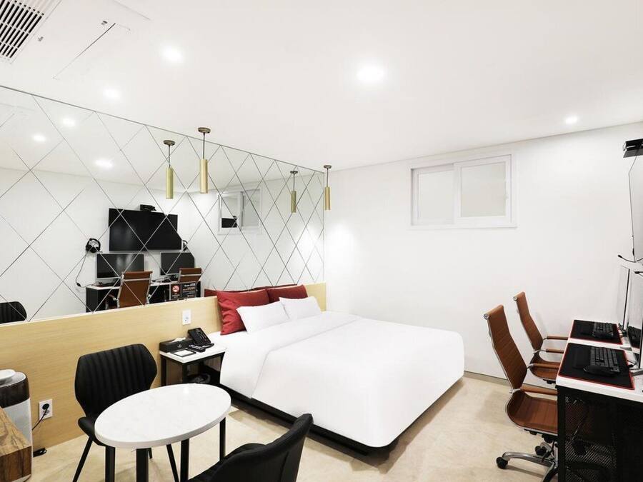 Une chambre d’hôtel comprenant un lit, un bureau avec un ordinateur, une chaise, une petite table, un miroir et un téléviseur.