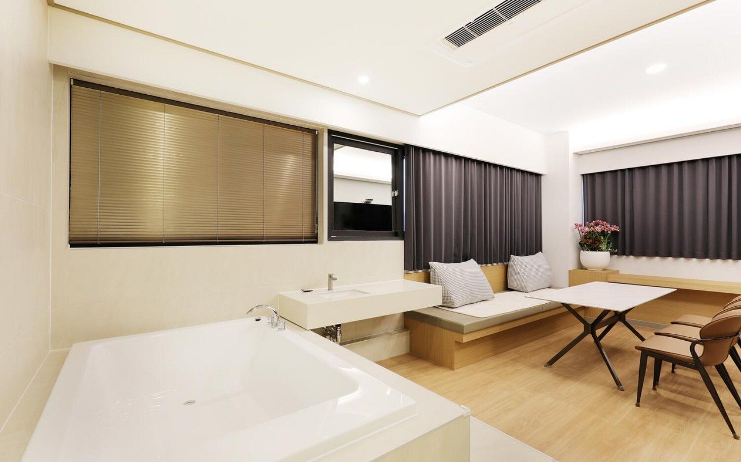 A modern bathroom with a bathtub, a vanity with a mirror, and a seating area with a table and chairs.