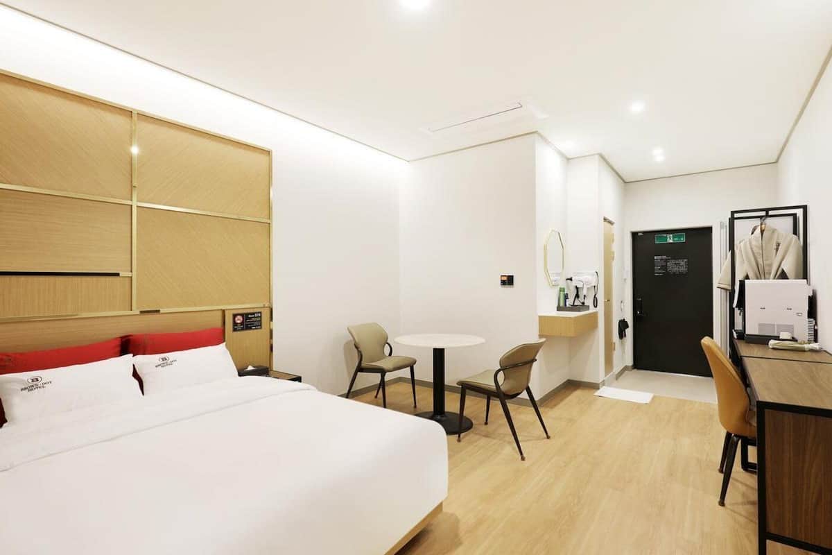 Une chambre d’hôtel avec un lit, un bureau, une chaise, une petite table et un miroir.
