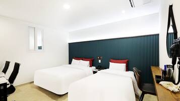 A hotel room with two beds, a desk, a chair, a mirror, and a camera on a tripod.