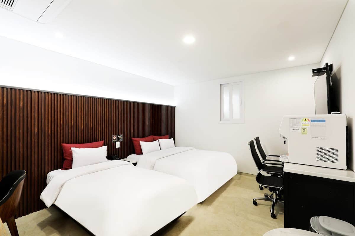 Une chambre d’hôtel avec deux lits, un bureau, une chaise, une télévision et un radiateur fixé au mur.