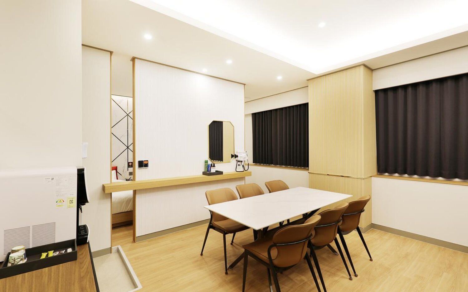 A hotel room with a large bed, a desk with a computer, a chair, a table with chairs, and a window with curtains.