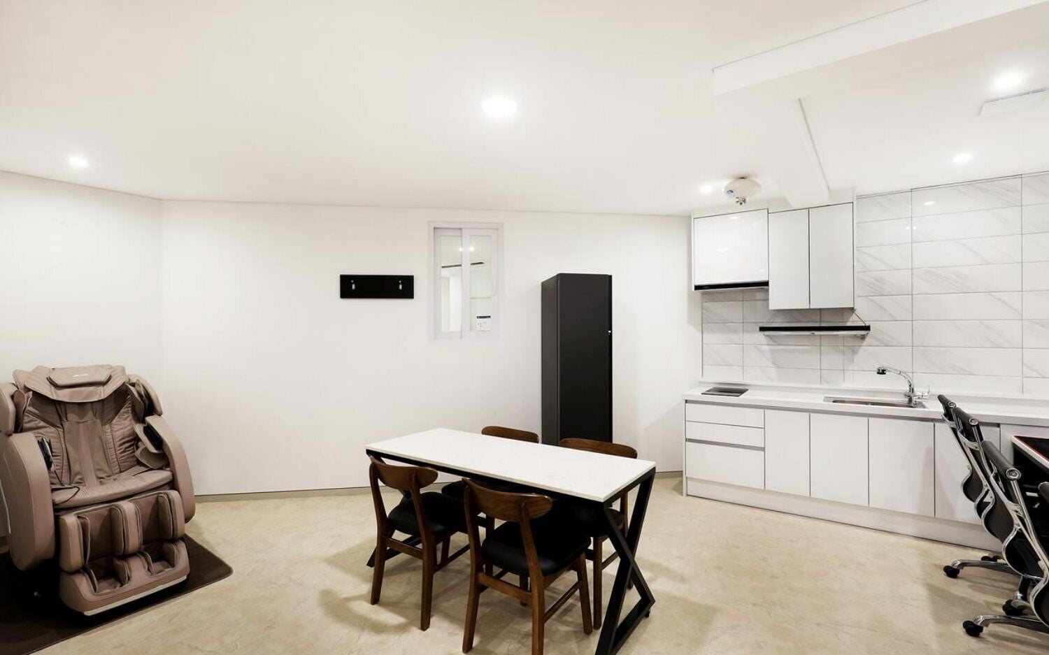 A modern kitchen with white cabinets, a black refrigerator, and a dining area with a table and chairs.