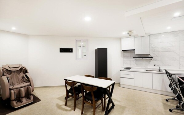 Une cuisine moderne avec des meubles blancs, un réfrigérateur noir et un coin repas comprenant une table et des chaises.