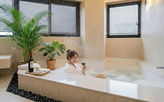 Una persona relajándose en una bañera con una planta en maceta y una botella de vino en la encimera.