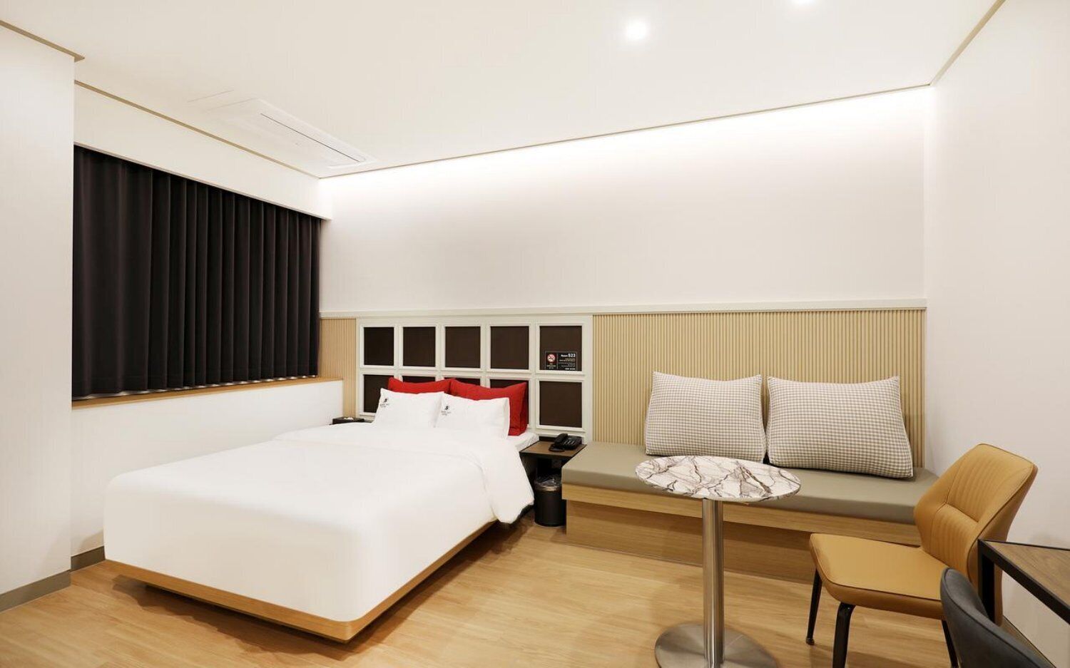 A hotel room with a bed, bedside table, chair, and a small table with a lamp.