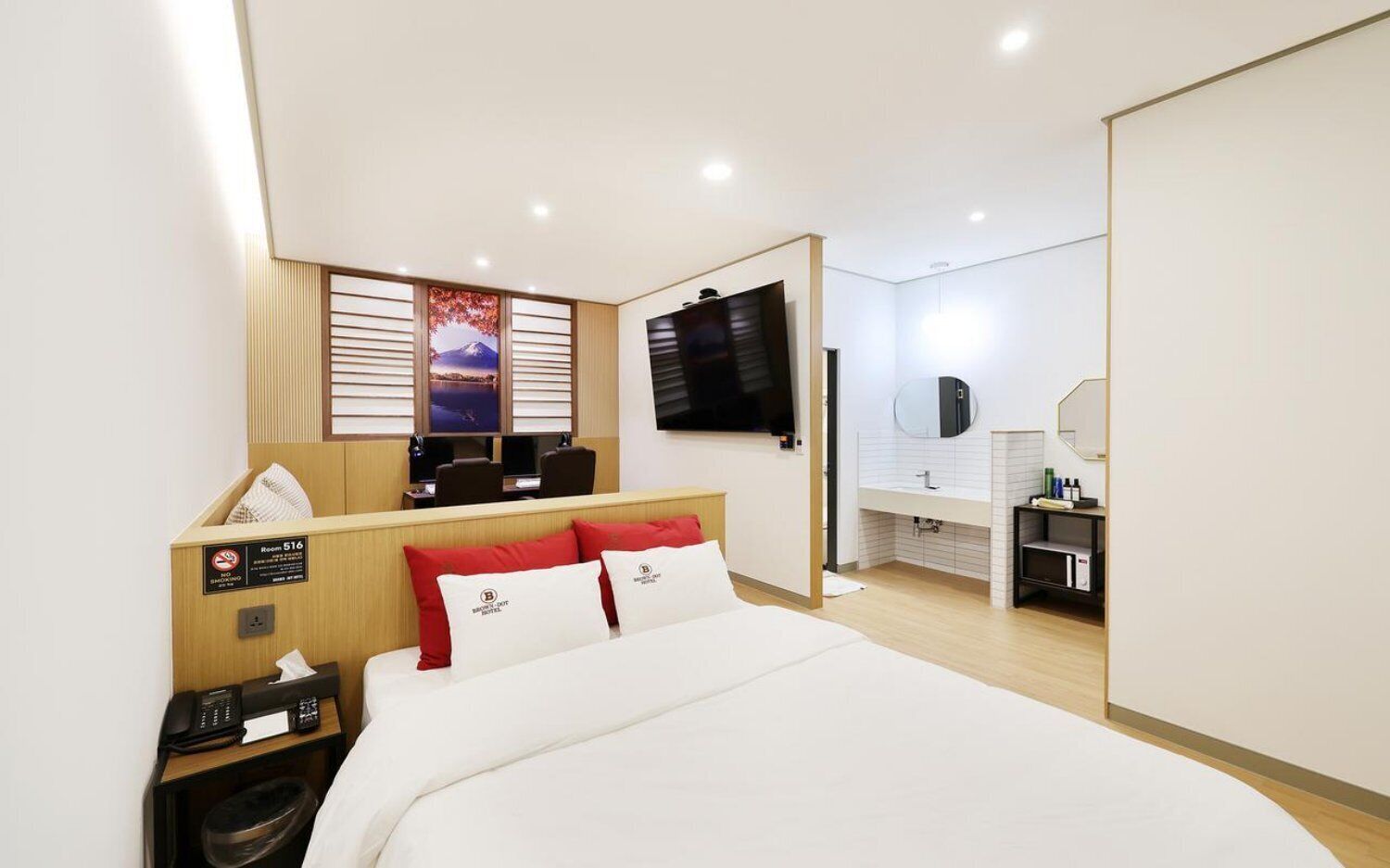 A hotel room with a bed, a desk with a computer, a TV, a bathroom with a mirror, and a view of a mountain.