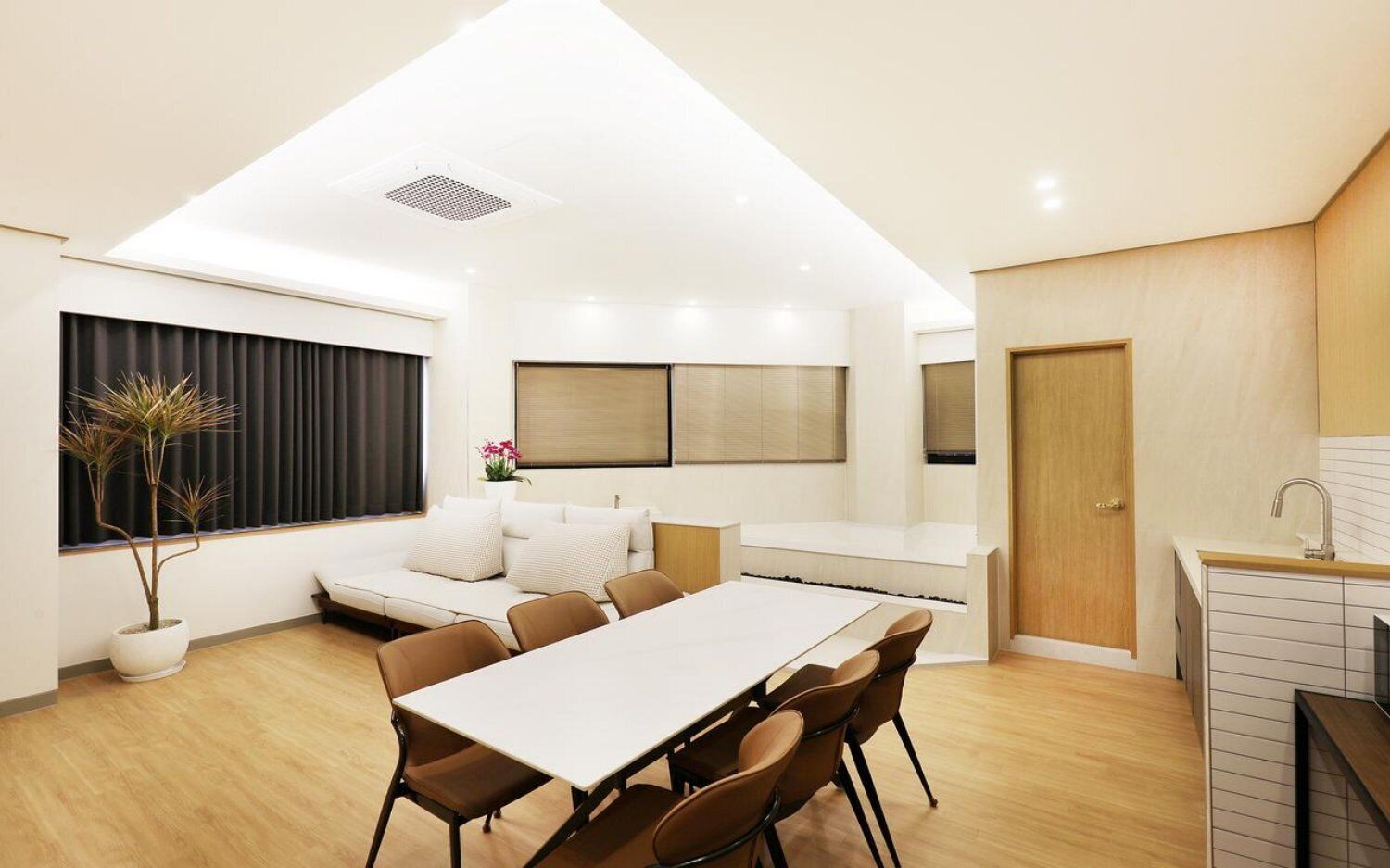 A modern interior with a dining area, a sofa, a potted plant, and a kitchen area.