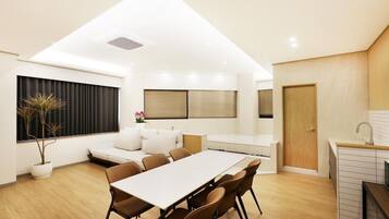 A modern interior with a dining area, a sofa, a potted plant, and a kitchen area.