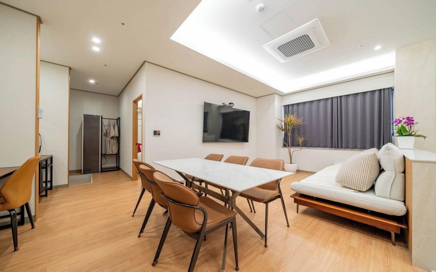 A modern room with a dining table, chairs, a sofa, a TV, and a window with curtains.