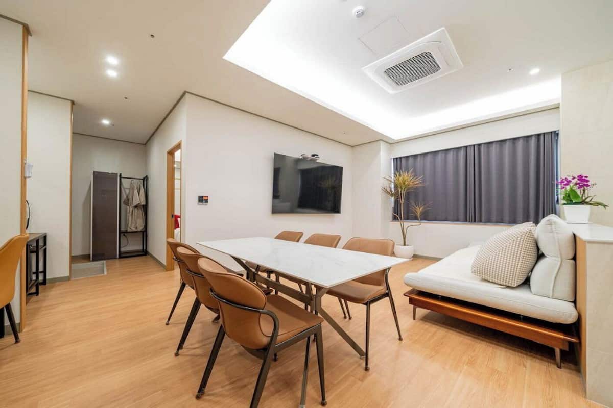 Une pièce moderne comprenant une table à manger, des chaises, un canapé, un téléviseur et une fenêtre avec des rideaux.