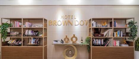 Zona de recepción de un hotel con un cartel que dice 'HOTEL BROWN DOT', estanterías de madera y objetos decorativos.