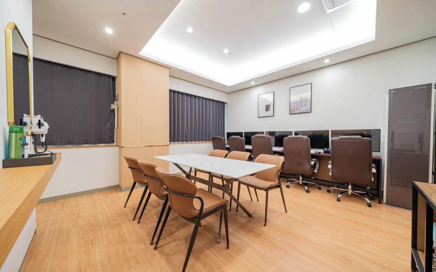 A modern conference room with a long table, multiple chairs, and a row of computers.