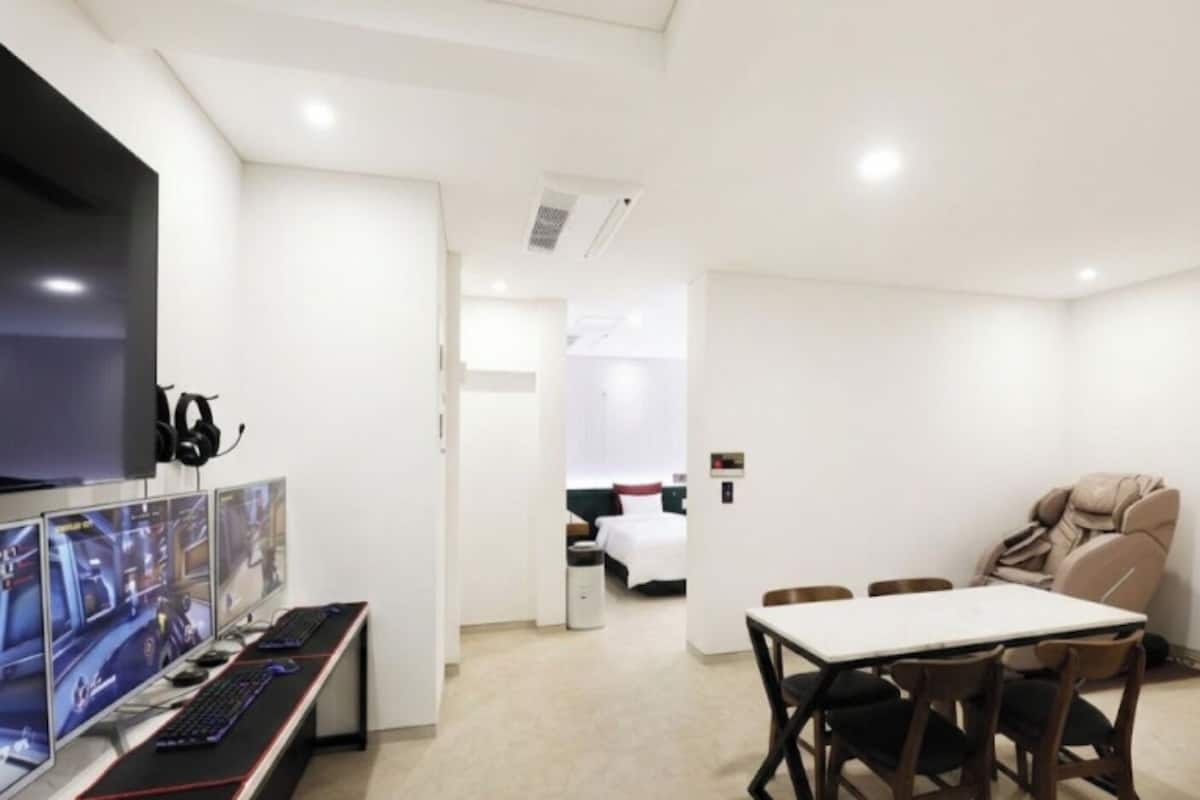 Une chambre d’hôtel moderne équipée d’un téléviseur à écran plat, d’écrans d’ordinateur pour les jeux vidéo, d’un fauteuil massant et d’une table à manger.