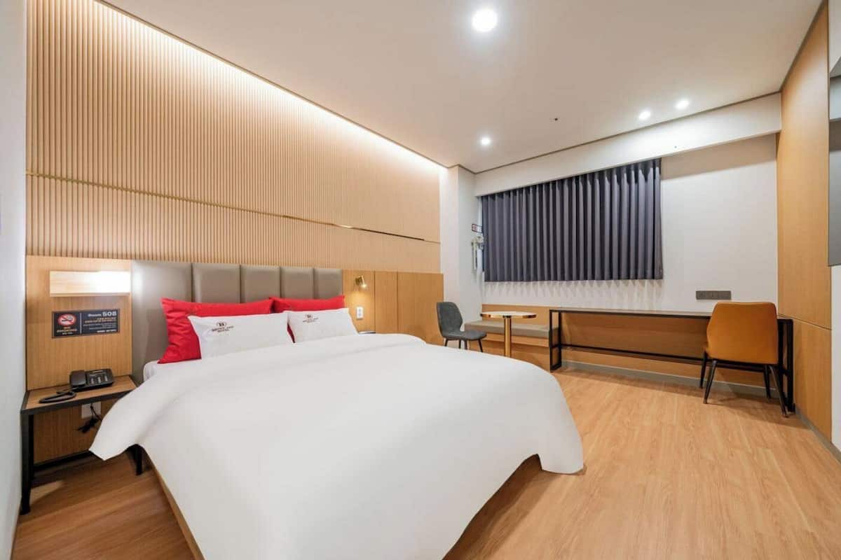 Une chambre d’hôtel équipée d’un lit, d’un bureau, d’une chaise, d’une table de chevet et d’un téléviseur fixé au mur.