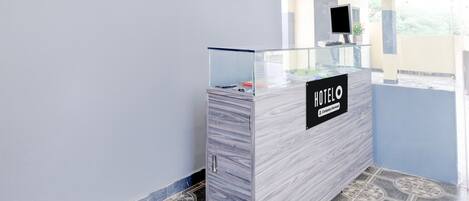 A reception desk with a glass top, a sign reading 'HOTEL', and a monitor on a stand.
