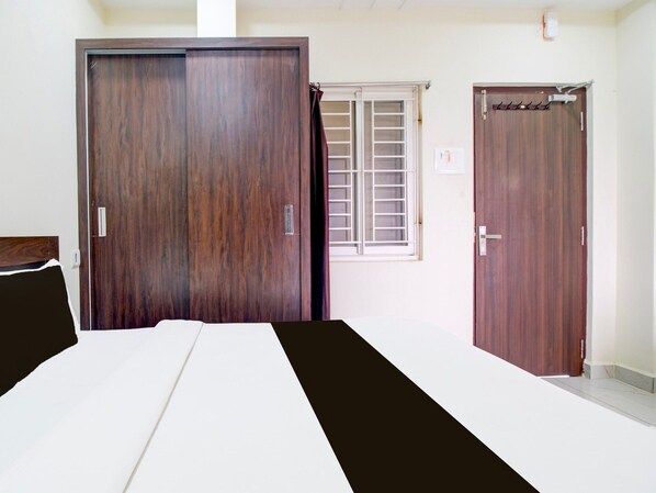 Une pièce avec un lit, deux portes en bois, une fenêtre avec des stores et un mur blanc.