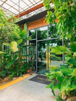 A greenhouse entrance with a 'WELCOME' mat, glass doors, and various tropical plants. - TAVANA Residence (Chalong)