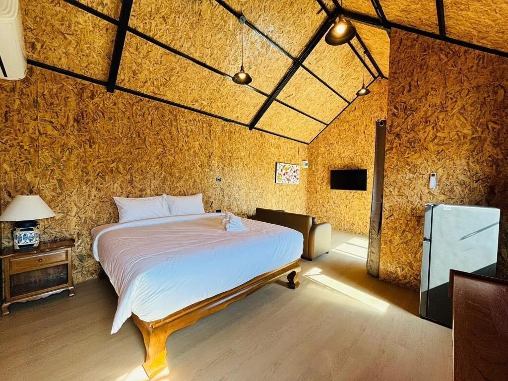 A bedroom with a wooden ceiling, a bed, a nightstand, a lamp, and a small table.