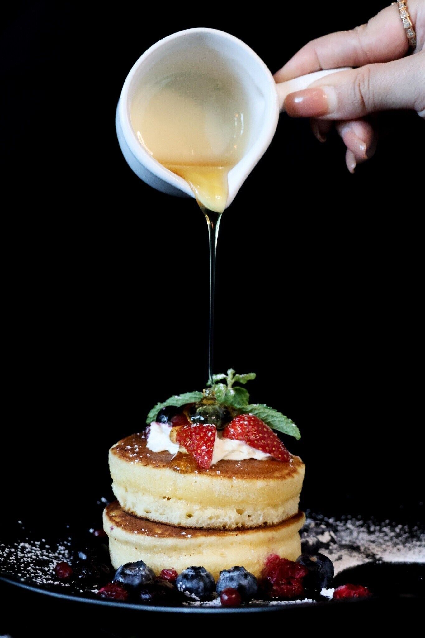 Ein Stapel Pfannkuchen mit darüberlaufendem Sirup, dekoriert mit Erdbeeren und Blaubeeren.