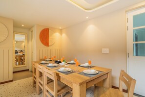 A dining area with a wooden table set for four, equipped with plates, glasses, and cutlery. - Elivaas Solace AquaVista 5BHK Villa (Candolim)