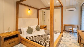 Una cama con dosel y estructura de madera, una mesita de noche con lámpara, una silla y una pequeña mesa con otra silla.