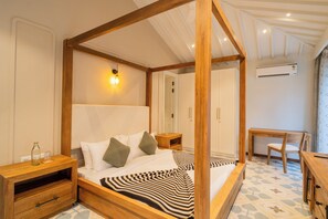 A four-poster bed with a wooden frame, a bedside table with a lamp, a chair, and a small table with a chair. - Elivaas Solace AquaVista 5BHK Villa (Candolim)