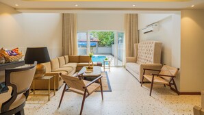 Amplia sala de estar con sofá, sillones, una mesa de centro y una mesa de comedor. Se ve una piscina a través de amplias ventanas.
