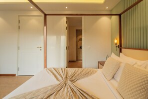 A bedroom with a bed, a nightstand, a wall-mounted lamp, and an open door leading to a bathroom. - Elivaas Solace AquaVista 5BHK Villa (Candolim)