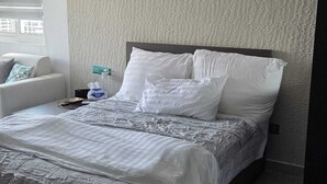 Un letto rifatto con lenzuola bianche, una coperta grigia a fantasia e una testiera.