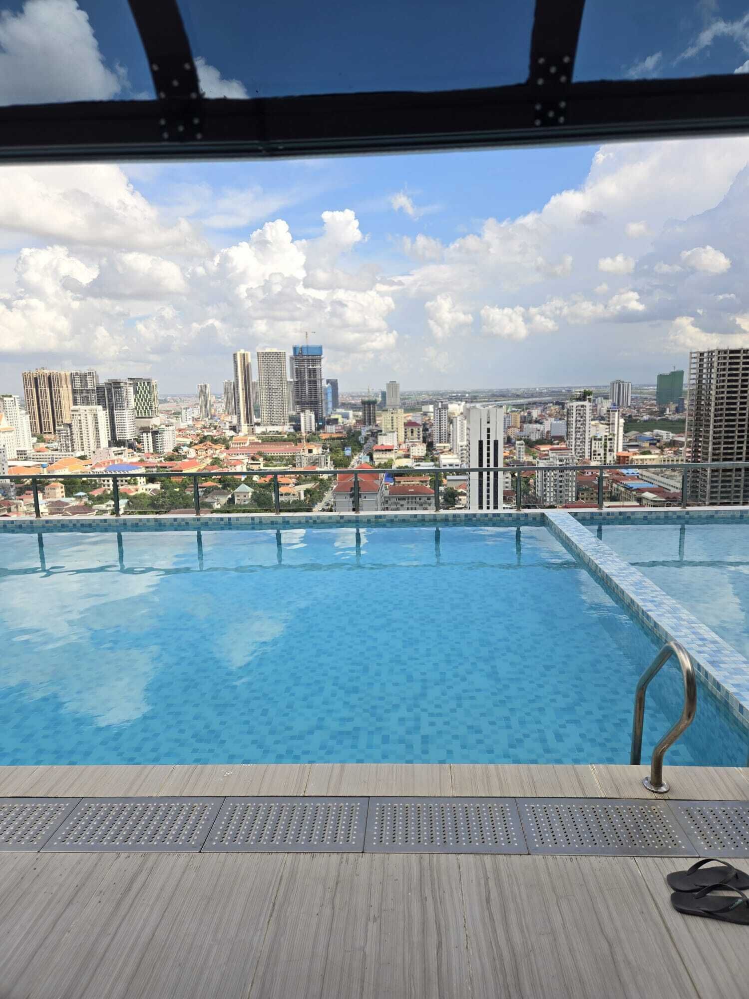 Une piscine sur le toit offrant une vue sur la ville, avec des garde-corps en métal et une terrasse en bois.