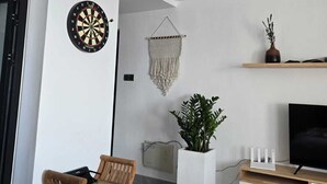 Un soggiorno moderno con un bersaglio da freccette, un arazzo in macramè, una pianta in vaso, un televisore e una sedia in legno.