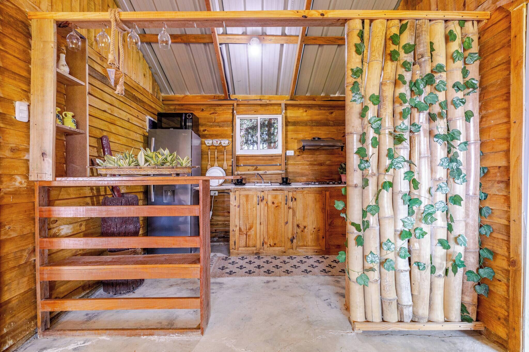 Une cuisine rustique, située dans une cabane en bois, avec un îlot central, une fenêtre et des éléments de décoration murale en bambou.