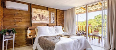 Une chambre avec un lit, des murs en bois, un appareil de climatisation, une fenêtre avec des rideaux et un balcon avec une table et des plantes.