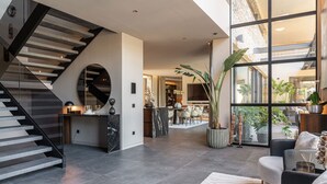 A modern interior with a staircase, a dining area, and large windows. - New build villa right on the beach with tropical garden and Bali feeling (Cala Vinyes)