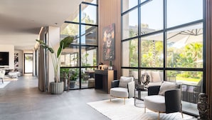 A spacious living area with large windows, a flat-screen TV, and a dining area with a table and chairs. - New build villa right on the beach with tropical garden and Bali feeling (Cala Vinyes)