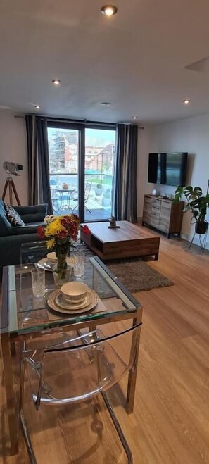 Un salon moderne avec une table à manger en verre, un canapé et un téléviseur fixé au mur.