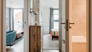 A bedroom with a bed, a wooden dresser, a mirror, and a window. - Beautiful 1 Bedroom Waterfront Apartment with parking in Gloucester Docks (Gloucester)