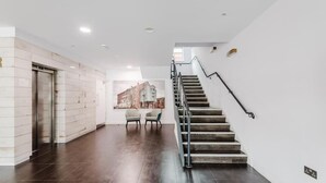 A modern interior with a staircase, a wall-mounted elevator, and a seating area with chairs. - Beautiful 1 Bedroom Waterfront Apartment with parking in Gloucester Docks (Gloucester)