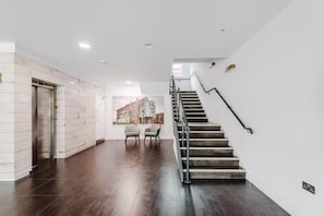Een modern interieur met een trap, een in de muur gemonteerde lift en een zithoek met stoelen.