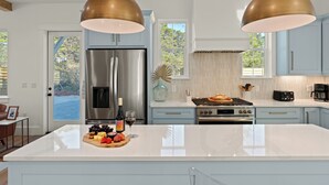 Une cuisine moderne dotée d’appareils électroménagers en acier inoxydable, d’un grand îlot central et de luminaires suspendus.