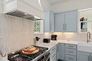 A modern kitchen with a gas stove, a coffee maker, and light blue cabinets. - Pool + Hot Tub + Game Room + Golf Cart + Bikes | Sleeps 26 | 30A Southern Sugar (Santa Rosa Beach)