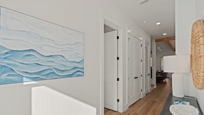 Un couloir avec des portes blanches, un plancher en bois et une œuvre d’art fixée au mur représentant des vagues.