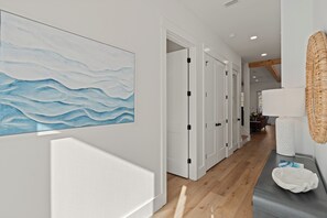 A hallway with white doors, a wooden floor, and a wall-mounted artwork depicting waves.
