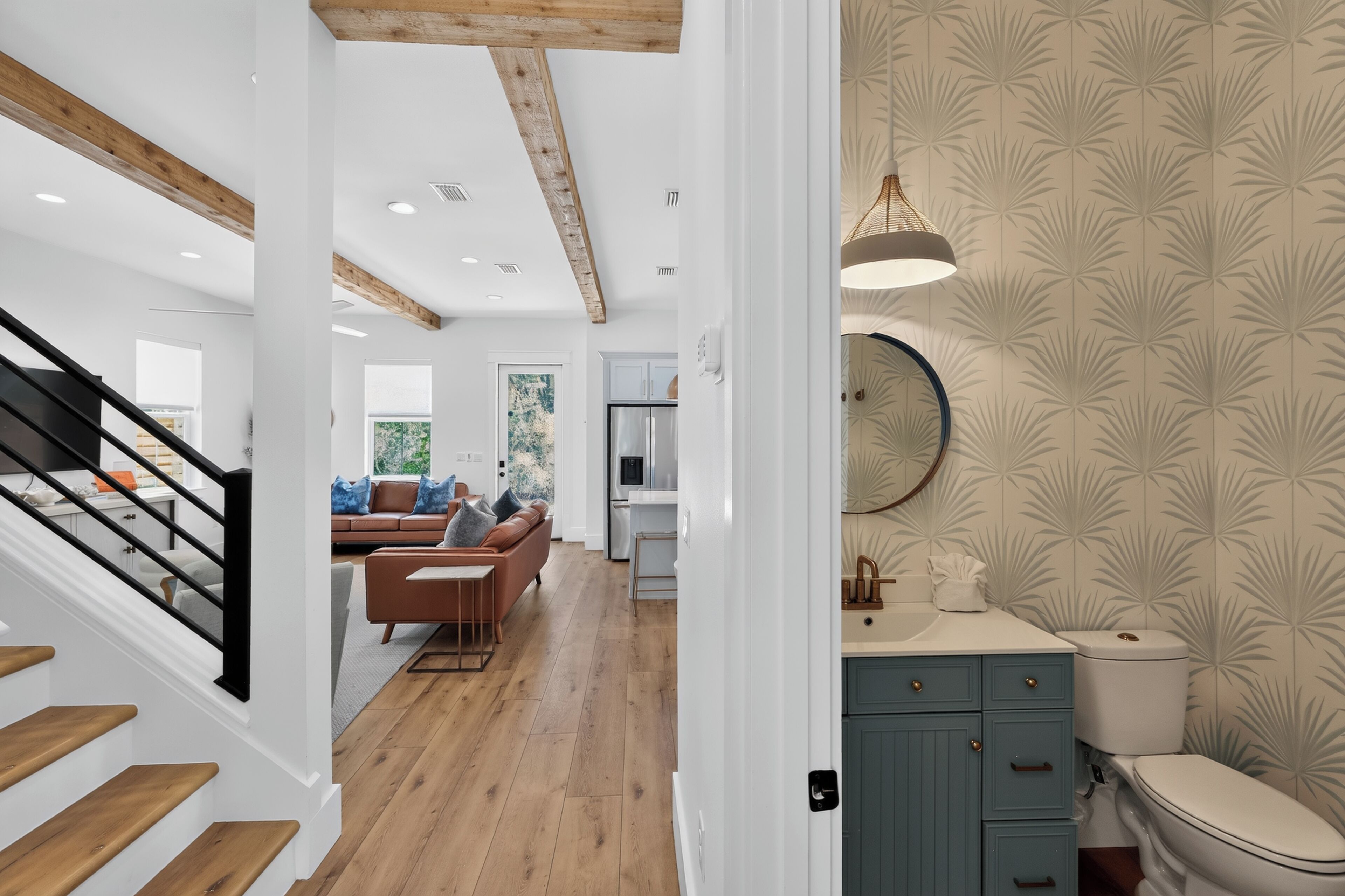 A modern interior with a staircase, wooden floors, a living area with a sofa, and a bathroom with patterned wallpaper.