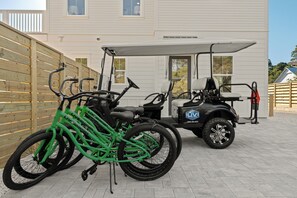 A golf cart, a green bicycle, and a wooden fence in a paved area. - Pool + Hot Tub + Game Room + Golf Cart + Bikes | Sleeps 26 | 30A Southern Sugar (Santa Rosa Beach)